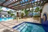 Inviting apartment complex featuring a sunlit pool and spa, framed by elegant pergolas and lush tropical landscaping.