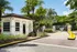 Welcoming entrance with lush palm trees and a charming guardhouse, featuring vibrant landscaping against a bright blue sky.