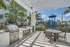 Modern outdoor kitchen and dining area with stainless steel grills and seating under a stylish pergola, next to a vibrant playground surrounded by lush greenery.