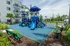 Modern apartment complex with a vibrant blue playground, surrounded by lush greenery and palm trees, perfect for family living.