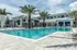Luxurious modern apartment complex with a stunning swimming pool, surrounded by palm trees and lounge chairs, under a beautiful blue sky.