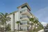 Modern apartment building with spacious balconies, surrounded by lush palm trees under a bright blue sky.