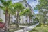 Charming exterior of a modern apartment building surrounded by lush palm trees and vibrant greenery, offering a tropical oasis feel.