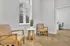 Elegant apartment corner featuring two modern leather chairs and a round wooden table, set against large windows with a serene view.