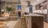 Elegant open-concept living room and kitchen with modern decor, featuring a sunset cityscape view through tall windows.
