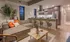 Modern open-concept living room and kitchen with stylish decor, featuring a cozy L-shaped sofa, elegant bar stools, and sleek stainless steel appliances.
