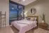 Modern bedroom with stylish decor, featuring a cozy bed with pink bedding, large windows showcasing a vibrant city view, and a sleek bedside table with elegant accessories.