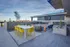 Modern rooftop terrace with vibrant yellow dining chairs, sleek white table, and cozy lounge area with outdoor TV and fire pit.