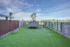 Modern rooftop terrace with lush grass, stylish planters, and stunning city views under a clear blue sky.