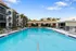 Elegant apartment complex with a luxurious swimming pool, surrounded by palm trees and stylish lounge chairs, under a vibrant blue sky.