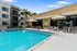Inviting apartment complex with a pristine pool, stylish poolside seating, and lush palm trees under a clear blue sky.