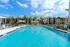 Inviting outdoor swimming pool with modern apartment buildings, lush palm trees, and blue skies, offering a tropical oasis for relaxation.