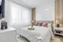 Elegant bedroom showcasing plush bed with soft pink accents, modern side tables, ambient lighting, and sheer curtains filtering natural light.