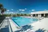 Luxurious apartment complex pool area with sun loungers and umbrellas, surrounded by lush palm trees under a clear blue sky.