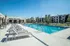 Inviting outdoor pool area with stylish lounge chairs and umbrellas, surrounded by lush landscaping and modern apartment buildings.