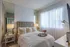 Cozy bedroom with elegant decor, featuring a plush bed with fluffy pillows, stylish lamps, and a sunlit window with sheer curtains.