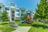 Modern apartment complex with charming playground and lush greenery under a bright blue sky, perfect for family living.