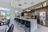 Luxurious modern kitchen featuring elegant pendant lighting, a spacious white island with plush navy stools, and sleek stainless steel appliances surrounded by large windows offering scenic views.