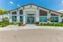 Elegant modern building exterior with a pitched roof, surrounded by lush landscaping and vibrant flowers under a clear blue sky.