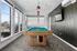 Bright and inviting recreational room with a sleek pool table, offering panoramic views through large windows, perfect for leisure and entertainment.