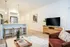 Chic open-plan living room featuring a modern kitchen with elegant pendant lighting, a stylish breakfast bar with seating, and a cozy seating area with a sleek TV stand.