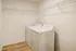 Bright laundry room with modern washer and dryer, featuring ample shelving and elegant wood flooring.