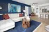 Elegant living room with a modern white sectional sofa against a navy blue accent wall, featuring abstract art. Includes a unique wooden coffee table, vibrant cushions, and open layout to a cozy dining area and sleek kitchen.