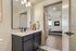 Modern apartment bathroom with sleek vanity and mirror, leading into a cozy, well-lit bedroom featuring contemporary furnishings.