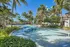 Luxurious tropical resort-style pool surrounded by lush palm trees and vibrant gardens under a clear blue sky.