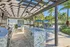 Chic outdoor kitchen and dining area with pergola, stone countertops, and lush palm tree surroundings.
