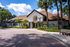 Exterior of a community leasing center with a covered arched entrance, brick-paved drive, and palm trees under a bright blue sky.