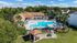 Aerial view of a resort-style swimming pool with lounge seating, surrounding apartment buildings, and lush landscaping on a sunny day.