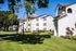 Exterior view of white apartment buildings with arched balconies, manicured lawns, walking paths, and mature trees under a clear blue sky.