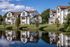 Apartment homes overlooking a tranquil pond with tree-lined banks and clear reflections under a blue sky.