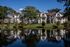 Waterfront apartment homes with arched architecture reflected in a serene pond, surrounded by trees and landscaped lawns.