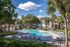 Resort-style swimming pool with lounge chairs, palm trees, and surrounding apartment homes on a clear, sunny day.