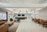 Open-concept resident lounge with multiple seating areas, bar counter, wall-mounted TVs, and abundant natural light.