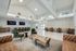 Open-concept resident lounge with multiple seating areas, bar counter, wall-mounted TVs, and abundant natural light.