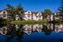 Apartment homes reflected in a calm waterfront setting with landscaped lawns and mature trees on a clear day.