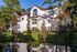 Waterfront apartment home with arched architectural details, surrounding trees, and reflections along a peaceful pond.