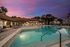 Main resort-style swimming pool at dusk with illuminated water, lounge seating, and surrounding clubhouse buildings.