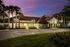 Community clubhouse exterior at dusk with illuminated windows, palm trees, and landscaped grounds.