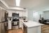 Modern apartment kitchen with stainless steel appliances, white cabinetry, quartz-style countertops, and a center island.
