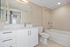 Modern bathroom with a white vanity, large mirror, toilet, and bathtub with beige subway tile walls.