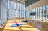 Sunlit yoga studio with wooden floors, mirrored wall, and exercise mats in a modern high-rise building.