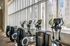Modern gym with elliptical machines lined up beside large floor-to-ceiling windows offering urban views.
