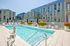 Rooftop swimming pool surrounded by lounge chairs, colorful flower planters, and modern apartment buildings.