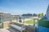 Rooftop area with artificial grass, a metal bench, glass railings, and city buildings in the background.