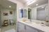 Modern bathroom with large vanity mirror, white quartz countertop, toilet, and glass walk-in shower.
