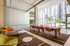 Contemporary workspace with large windows, orange chairs at communal tables, lounge seating, and views of a landscaped courtyard.
